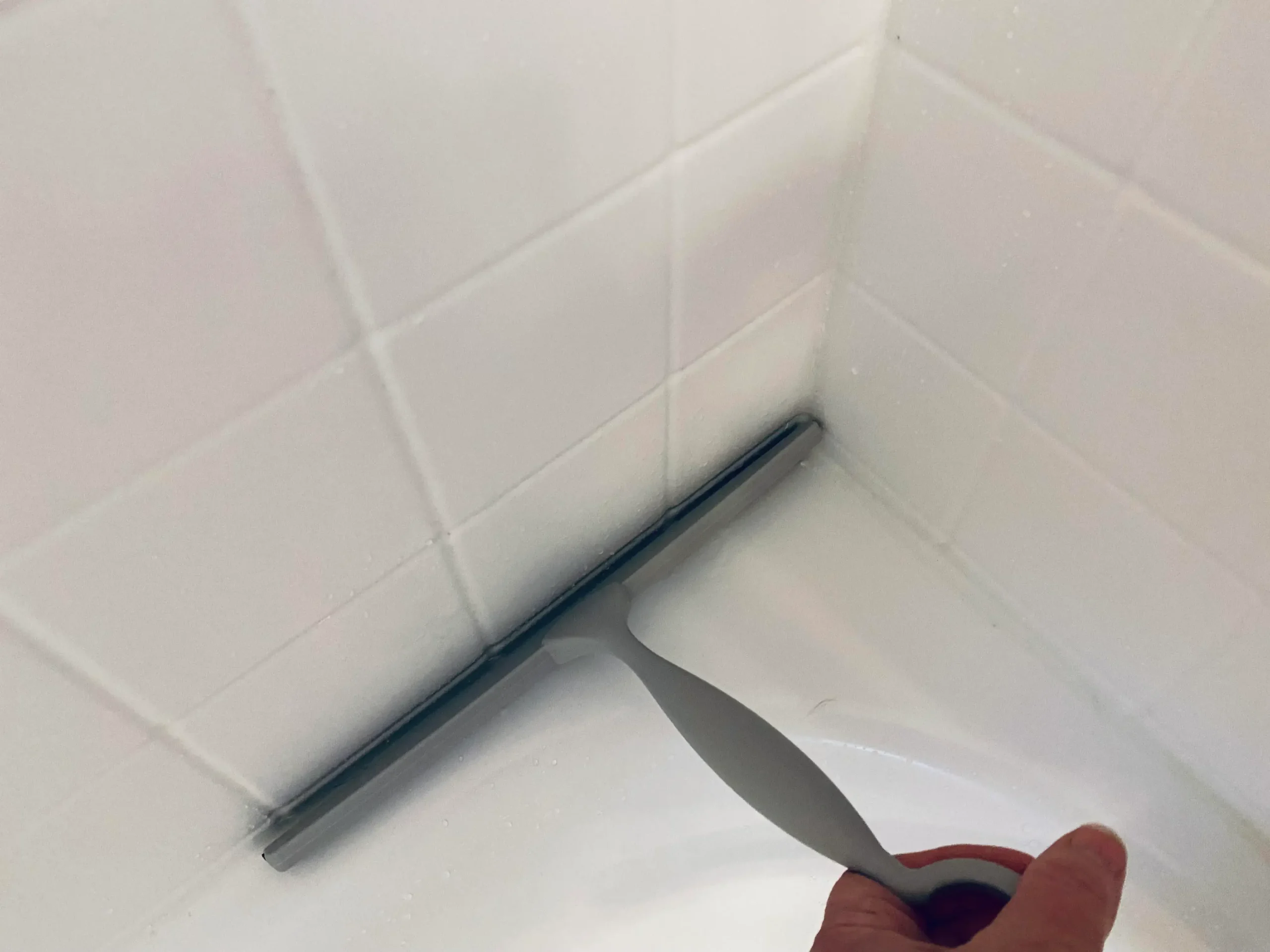 Person using a squeegee to wipe water off shower glass after a shower to prevent mold